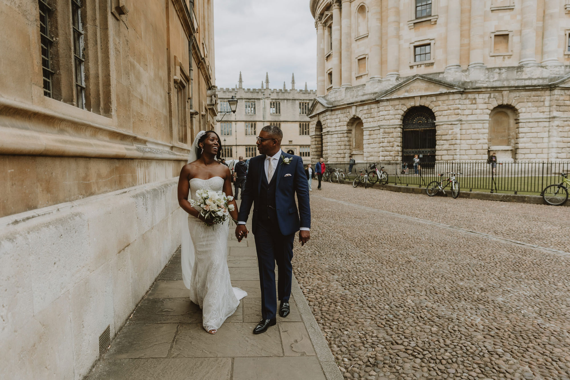 Wedding couple walk alongside The Radcliffe Camera in Oxford after their wedding