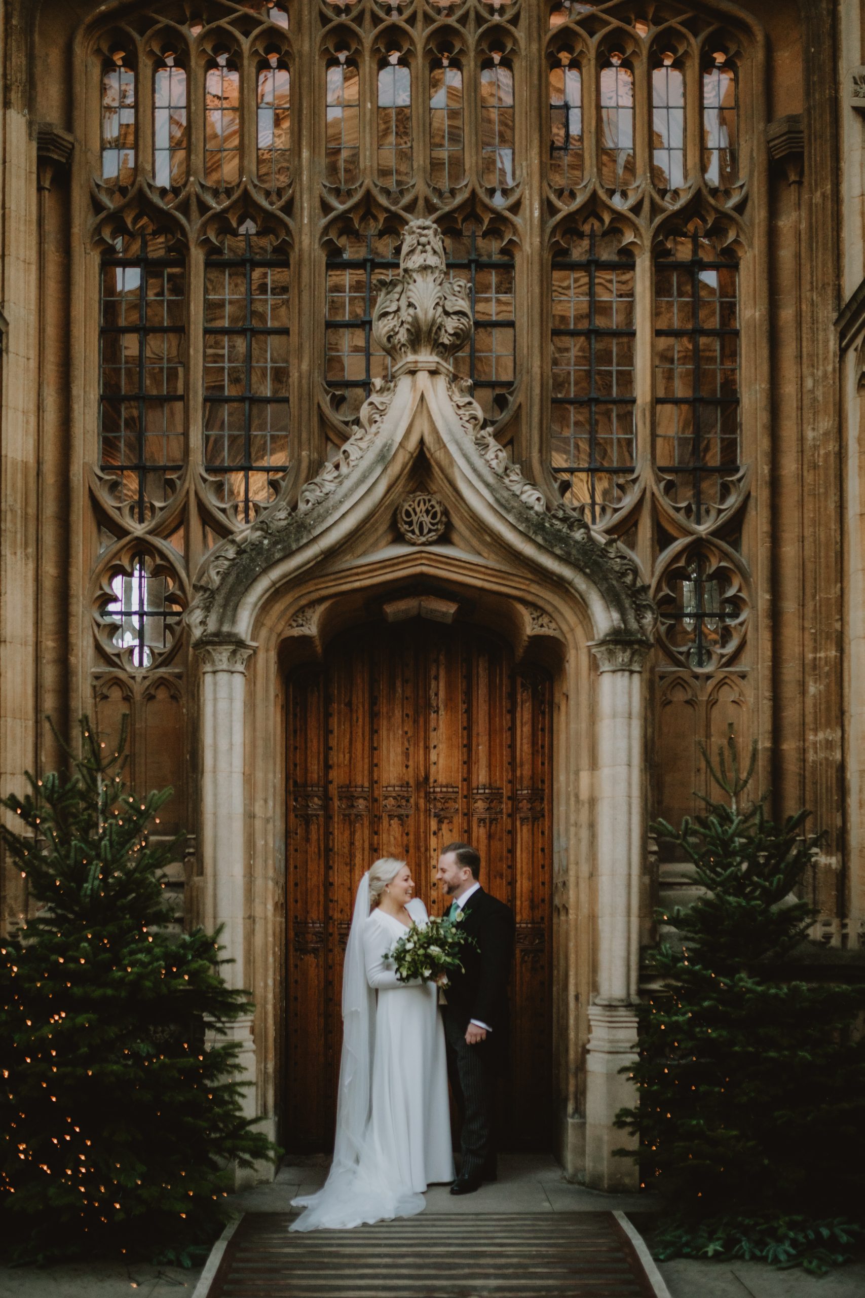 Wedding Couple stand in front of the Wren Door Divinity School Bodleian LIbrary with Christmas trees